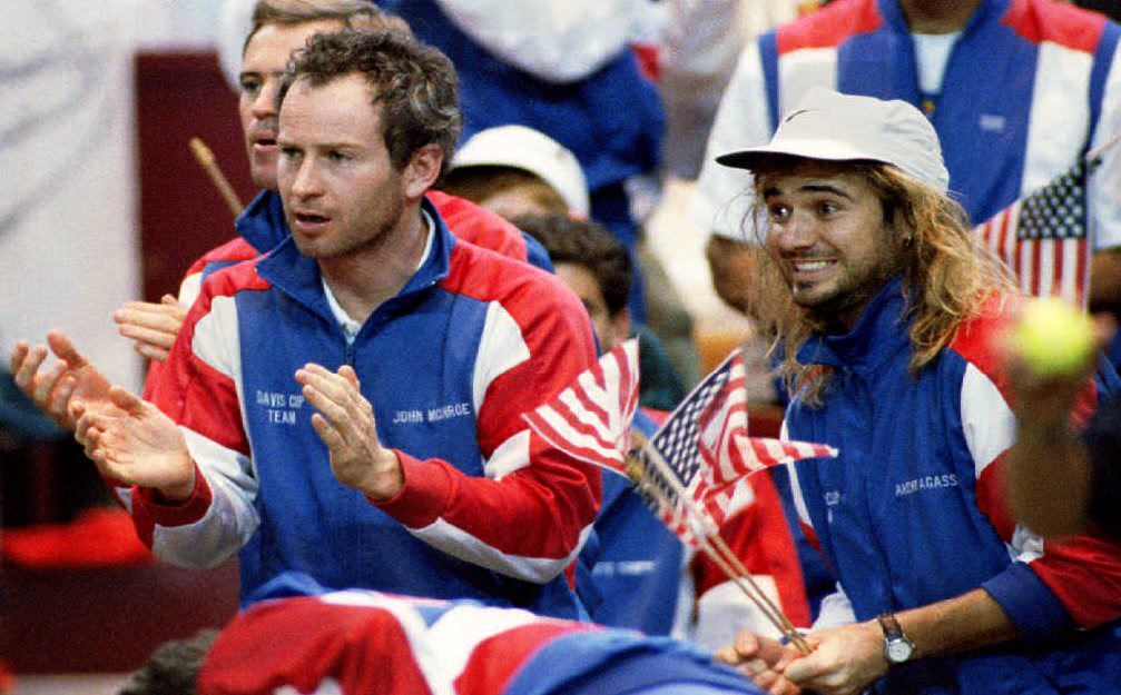 U.S. tennis players John McEnroe (L) and Andre Agassi cheer for teammate Jim Courier as he plays Switzerland's Marc Rosset in the second match of t...